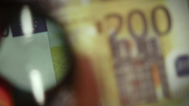 Front side of two hundred euro banknotes examine with magnifying glass, concept of counterfeit money and finance