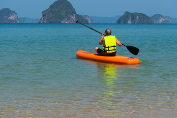 senior asian man playing paddle board in blue sea during summer vacation