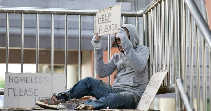Homeless man sitting and holding help please sign on the overpass