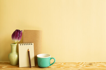 Fototapeta na wymiar Notebook, colored pencil, tulip flower, mug cup on wooden desk. beige background. Work and study place