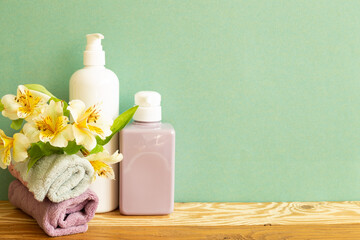 Fototapeta na wymiar Skin care and spa concept. Bathroom bottles and towel with yellow flowers on wooden shelf. green background