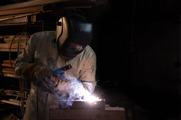 A welder is welding steel in an industrial factory. The welder wears protective clothing to work in the workplace.