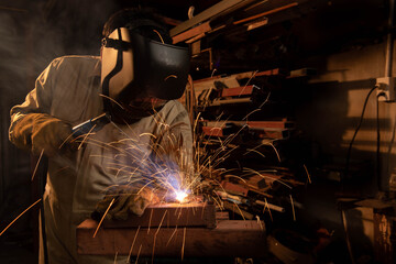 A welder is welding steel in an industrial factory. The welder wears protective clothing to work in the workplace.