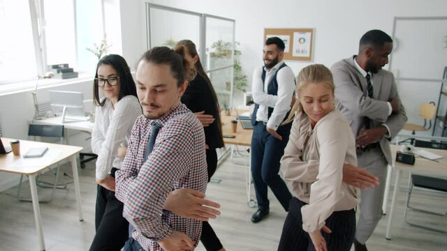 Slow motion of happy office workers multiracial team dancing together moving arms smiling in workplace. Cheerful employees and entertainment concept.