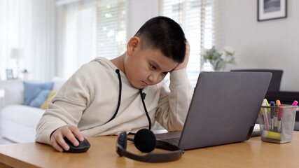 Young asia boy kid sit on desk look at computer notebook feeling bored tired and sleepy in remote...