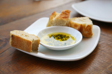 Bread with Olive Oil and Herbs on a white plate at a resturant. Appitizer of Fresh Bread with Olive...