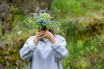 Fototapeta na wymiar The girl covers her face with a bouquet of wild forest flowers.