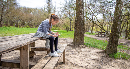 Fototapeta premium A little girl is sitting with a phone in her hands in the forest.