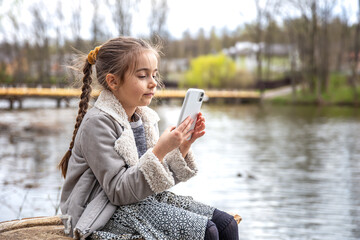 A little girl looks into the phone on a walk in the park.