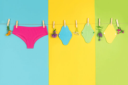 Panties and bamboo charcoal washable sanitary napkins on washing line. Healthy women's sanitary pads, reusable menstrual pads and natural flowers. Health care, zero-waste, eco-friendly concept