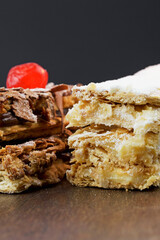 Puff pastry cakes with powdered sugar and cream and another with chocolate and a cherry on top on the wooden table. Close up and space for text. Selective focus. Vertical.