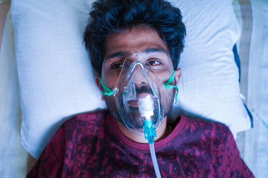 Top View Of Young Man Breathing On Ventilator Or Oxygen Concentrator Mask At Hospital Due Coronavirus Covid-19 Dyspnea Or Shortness Of Breath - Concept Of Covid Viral Infection Millennial People.