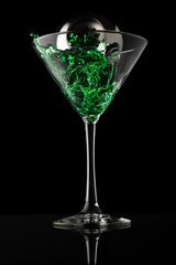 Martini glass with silver shaker pouring green liquid on a black background