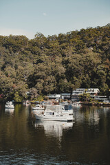 Obraz premium Boats on the water in front of idyllic waterfront houses at Berowra Waters NSW. As seen from the Great North Walk.