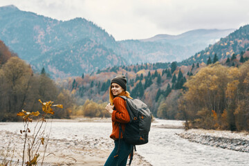 woman in a jeans sweater with a backpack rest in the mountains near the river in nature