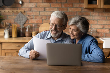 Happy middle aged couple holding paper read good news in document. Mature spouses checking bills,...