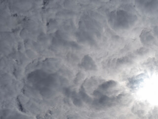 Solid gray-white Cumulus Clouds through which the Sun breaks through. Cloudy natural background