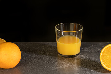 a glass of freshly squeezed orange juice and oranges on a dark background