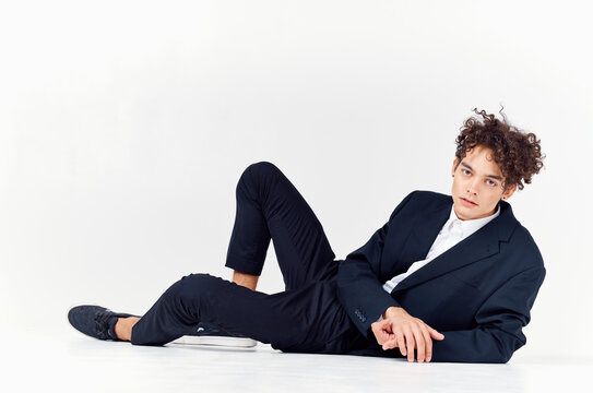 a man with curly hair lies in a suit on the floor in a bright room and sneakers style