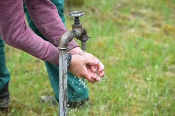 A worker in work overalls washes his hands over the water in natur