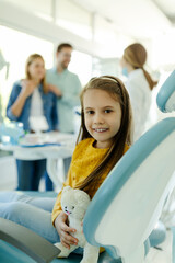 Little girl in dental office showing milk tooth while parent is discussing with dentist doctor.