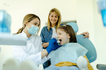 Doctor with mask shows to girl and parents how the prosthesis is used and how it affects the teeth.