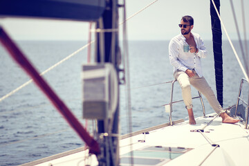 A young handsome male model is enjoying the sun and coffee at a photo shooting on a yacht on the seaside. Summer, sea, vacation
