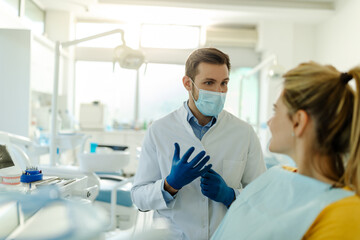 Photo of male dentist in dental office talking with female patient and preparing for treatment.
