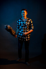 A guy in a plaid shirt with a dust brush on a dark background illuminated by blue and yellow light