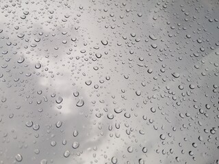 Raindrops on window glasses with cloudy sky background.