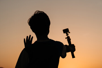 Fototapeta na wymiar Silhouette of an Indian teen vlogging while holding camera in his hand. Teenager vlogging for social Media. Young teen holding camera and speaking at the camera