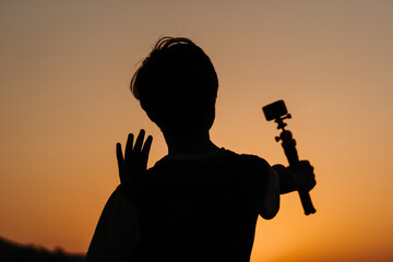 Silhouette of an Indian teen vlogging while holding camera in his hand. Teenager vlogging for social Media. Young teen holding camera and speaking at the camera