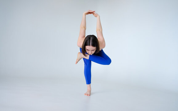 Portrait of sporty woman doing Kapotasana or standing Pigeon Pose. Attractive young woman training yoga on white background isolated on cyclorama.
