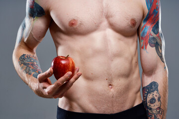 Naklejka premium male athlete with an apple in his hands and tattoo cubes on his stomach biceps press
