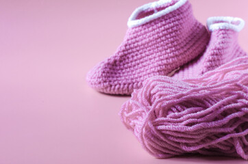 Fototapeta na wymiar A skein of pink yarn with knitted shoes on a pink kopi space background. Home knitting.