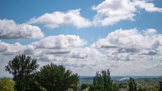 Fast Moving Clouds over Tops of Green Trees, Roofs of Houses, a Factory. Time Lapse. Forming, of gray rain clouds. Swirling clouds in the blue sky. Atmospheric phenomenon of nature. Time-lapse. 4K.