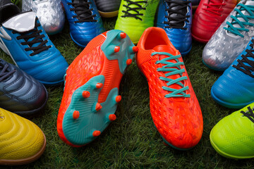 orange soccer shoes lie on the grass surrounded by many colored soccer shoes