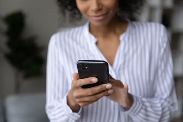 Crop close up of African American female user hold cellphone browse wireless internet on device. Mixed race female use smartphone text message online on gadget. Technology, communication concept.