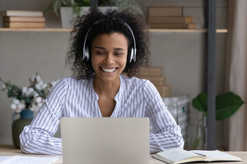Smiling young African American woman in earphones talk speak on video call on computer at home....