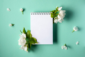 Empty notebook with spring flowering branches on a turquoise background. Flat lay. Top view.