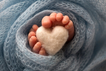 Two cute tiny baby feet wrapped in a blue-green aqua knitted blanket. And a knitted heart made of woolen threads.