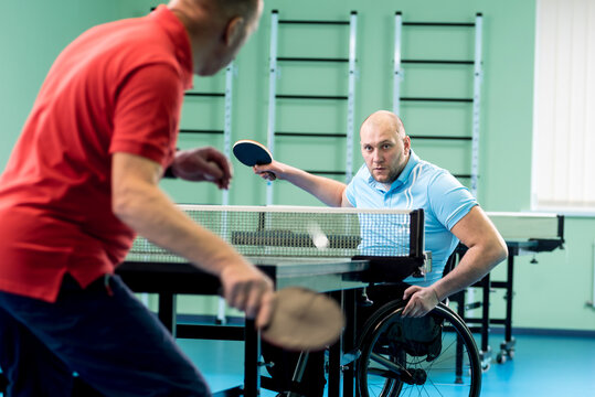 Adult disabled man in a wheelchair play at table tennis with his coach