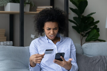 Fototapeta na wymiar Unhappy mad young African American woman have problems paying online on smartphone with credit debit card. Angry biracial female buyer frustrated by error or mistake shopping online on cellphone.