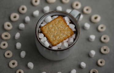 a gray ceramic mug, marshmallows and cookies in a mug, a pattern of marshmallows and cereal is...