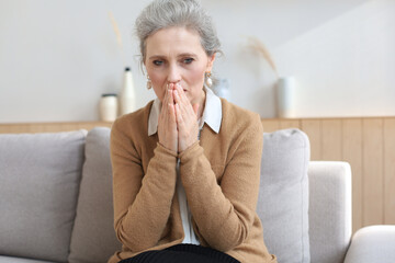 Worried middle aged woman sitting on a sofa in the living room.