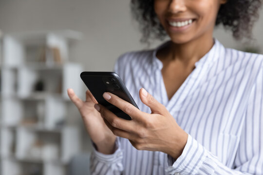 Crop close up of happy African American woman use cellphone text message online on gadget. Smiling mixed race female user hold smartphone browse good wireless internet on device. Technology concept.