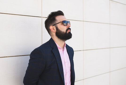 Bearded businessman is wearing sunglasses and leaning on the wall