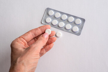 Round white pills in a woman's hand on a white background close-up.
