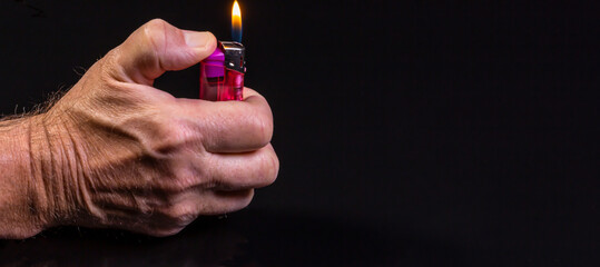 A male hand holding a red striked lighter on a black background - copy-space - obrazy, fototapety, plakaty