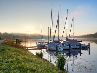 Obraz premium A wonderful sunrise over Lake Baldeneysee in the city of Essen. Moored sailboats in the foreground. Landscape photography